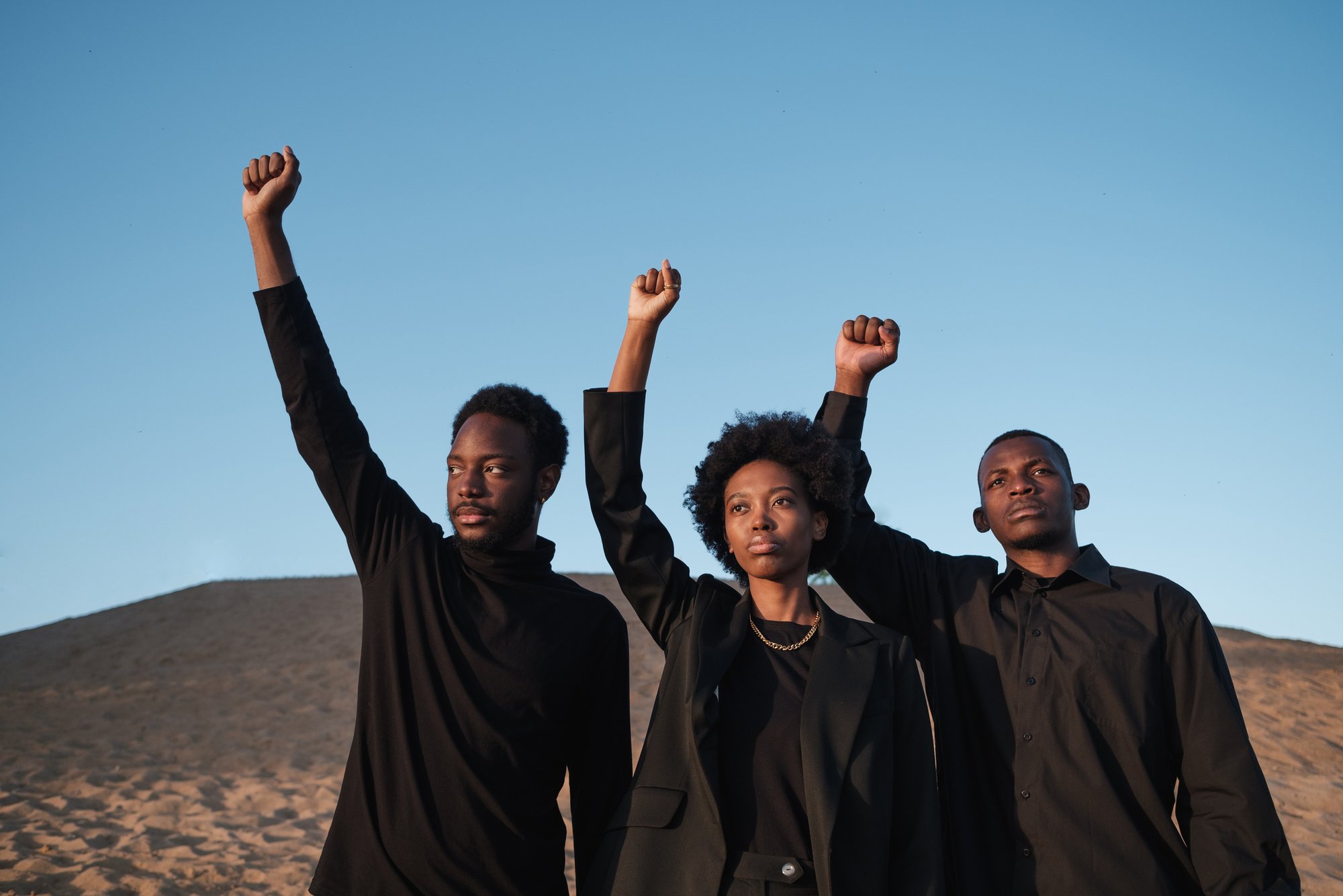 Three Diverse People in Black Outfit Raising Their Fist Outdoors